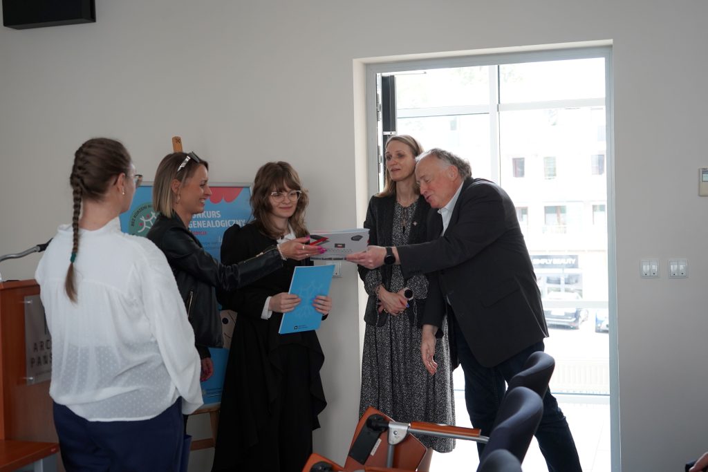 Mężczyzna wręcza dyplom finalistce konkursu. Obok niej stoi mężczyzna i dwie kobiety. 