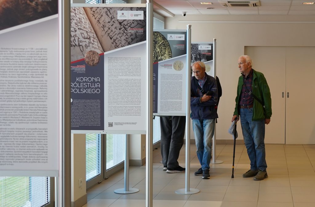 Kilka osób ogląda wystawę na planszach. 