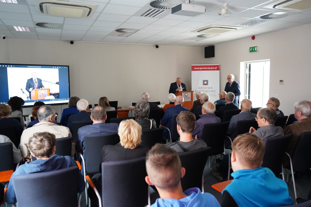 Spotkanie w sali konferencyjnej. Mężczyzna przemawia do zgromadzonych gości.