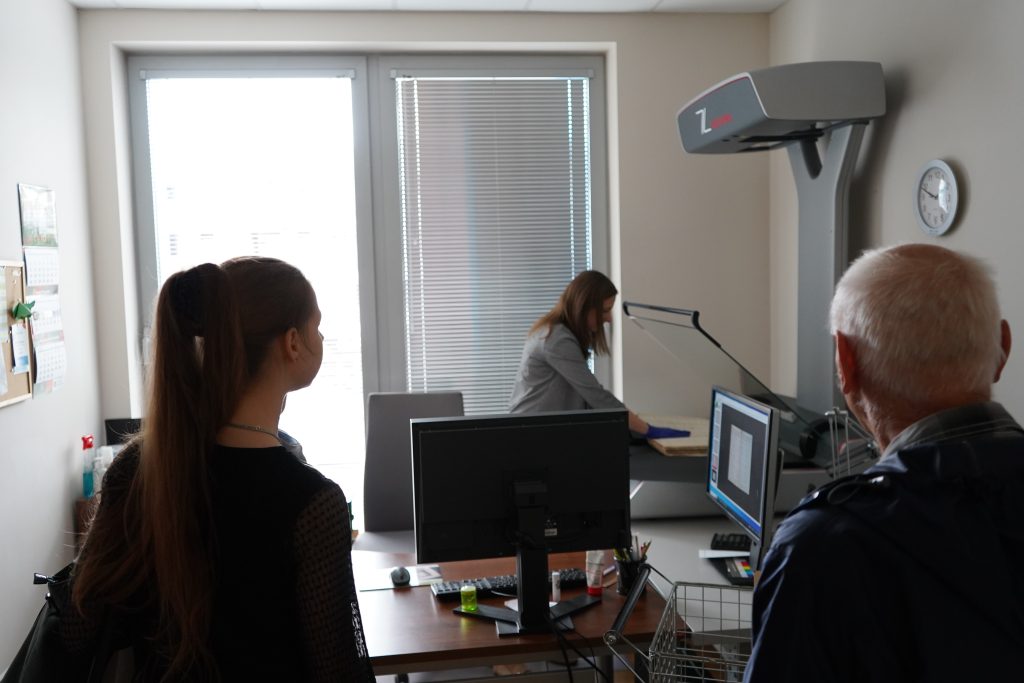 Zwiedzanie pracowni digitalizacji. Kobieta pokazuje działanie skanera.