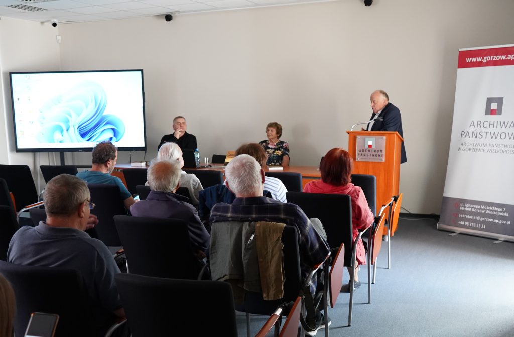 W sali konferencyjnej mężczyzna przemawia do zgromadzonych gości.