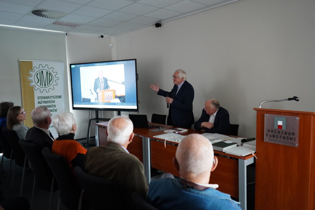 Spotkanie w sali konferencyjnej. Mężczyzna przemawia do zgromadzonych gości.