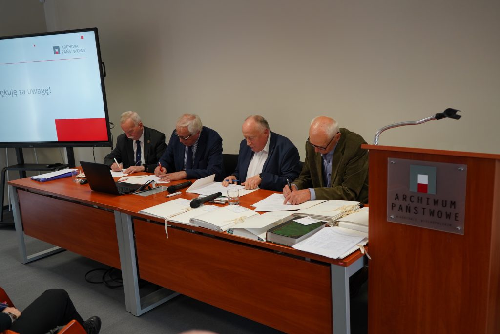Czterej mężczyźni siedzą przy stole i podpisują dokumenty.
