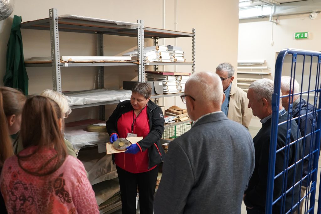 Zwiedzanie magazynów archiwalnych. Kobieta pokazuje taśmę szpulową.