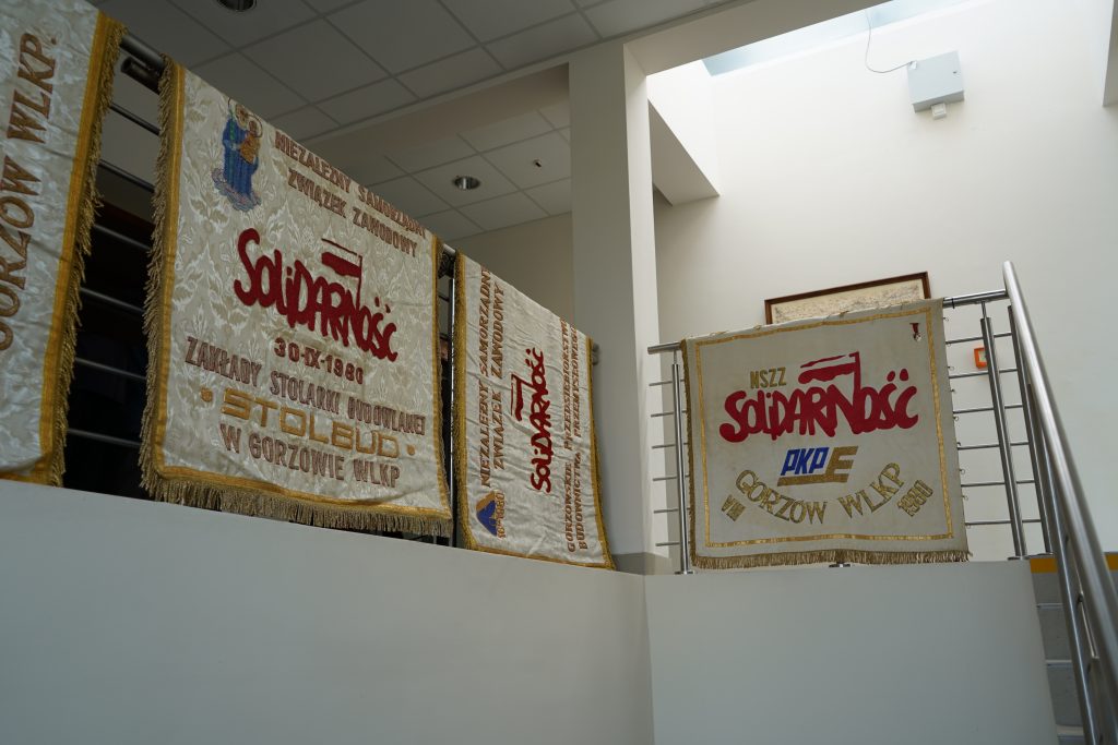 Widok na klatkę schodową. Na barierce wiszą sztandary Solidarności