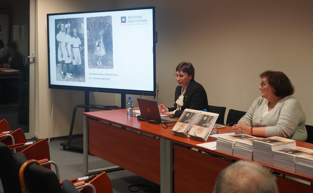 Za stołem siedzą dwie kobiety. Jedna z nich przemawia. Obok wyświetlany jest slajd na telewizorze. 